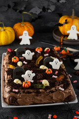 Halloween chocolate cake. Dirty cake with chocolate cream, decorated with worms, skulls, ghosts, pumpkins and sugar sprinkles on a dark background.