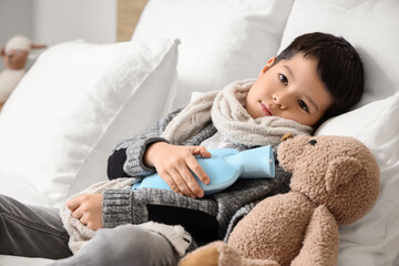 Ill little Asian boy with hot water bottle lying in bedroom