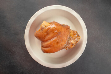 Cooked pork knuckle served in white plate on dark rustic background. top view