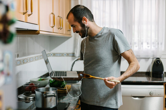 Mid adult man cooking while video conferencing on laptop at home