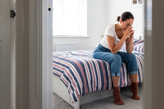 Stressed woman sitting on bed at home