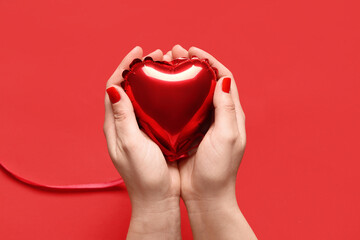 Female hands with red manicure and heart shaped balloon on color background. Valentine's Day...