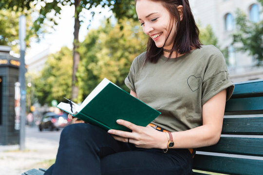 Portrait of smiling young woman sitting on bench reading a book