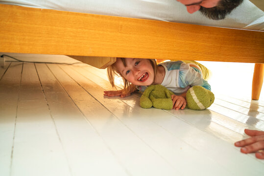 Cheerful girl hiding under bed at home