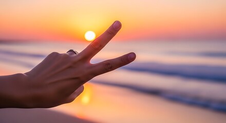 A person's hand making a peace sign against a beautiful sunset over the ocean.