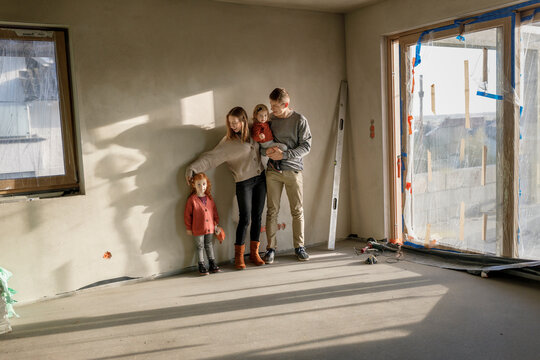 Siblings with parents standing in front of wall at incomplete home