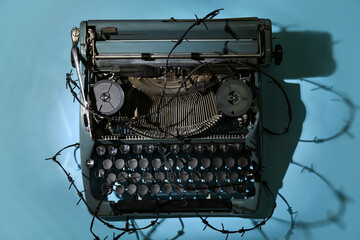 Vintage typewriter with barbed wire on blue background. Printing ban concept