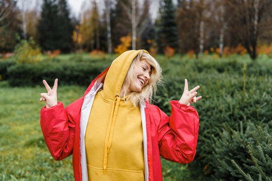 Playful woman wearing raincoat and showing peace sign in park
