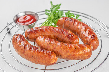 Grilled sausages with ketchup and parsley served on metal rack over white background