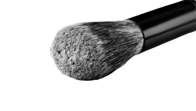 Close-up of a makeup brush tip, showing a textured, light gray powder or product densely packed into the brush bristles.  Black handle