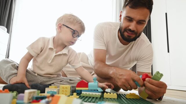 Father is playing in the room with his little son with construction sets.