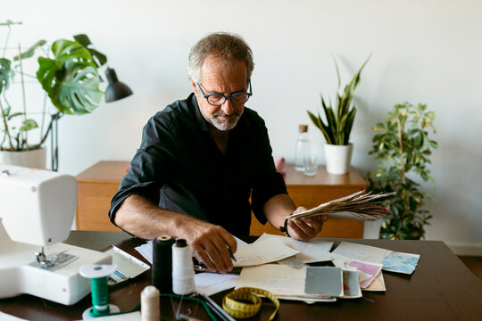 Male costume designer looking at documents while sitting at table in work studio