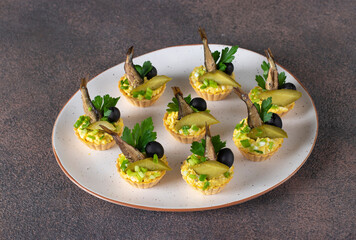 Tartlets with sprats, egg and pickled cucumber on light plate