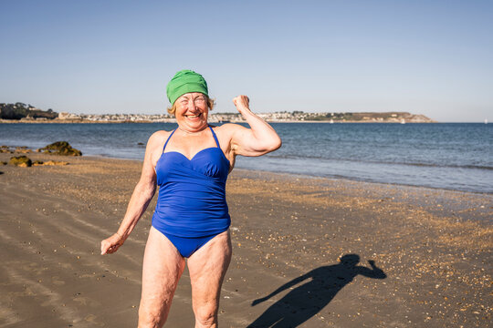 Happy senior woman flexing muscle at beach