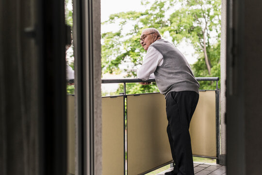Curious senior man standing on balcony watching something