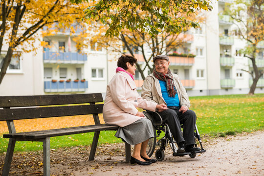 Senior woman sitting on bench next to husband in wheelchair