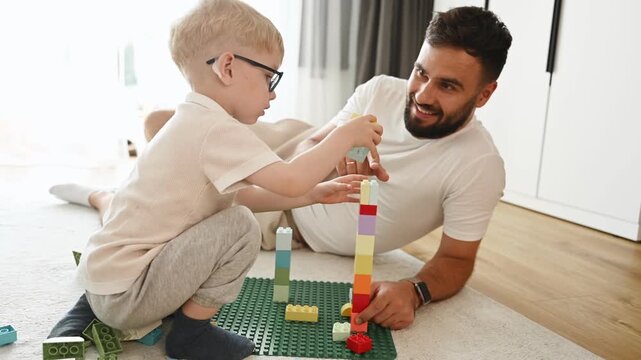 Father is playing in the room with his little son with construction sets.