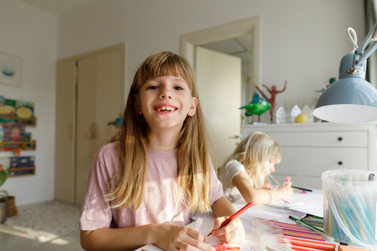 Happy girl drawing on paper with sister sitting in background