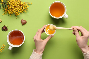 Young woman adding honey into tea on green background