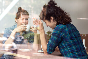 Two laughing women sitting behind windowpane of a coffee shop