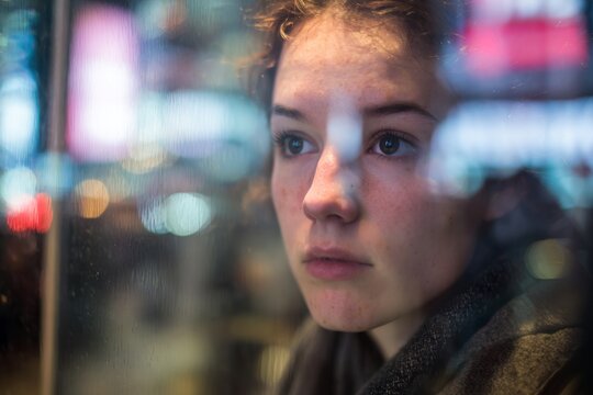 A person gazes intently at their reflection amidst the vibrant city backdrop, lost in contemplation during a bustling day. The atmosphere is lively yet introspective