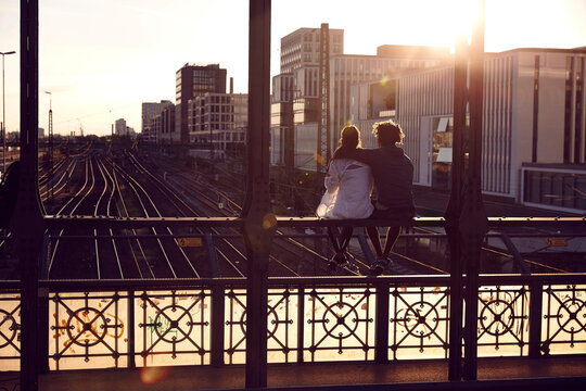 Germany, Munich, Young couple sitting on bridge, enjoying sunset