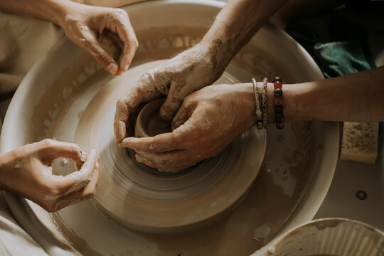 Hands of Instructor teaching young man molding bowl on potter's wheel in workshop