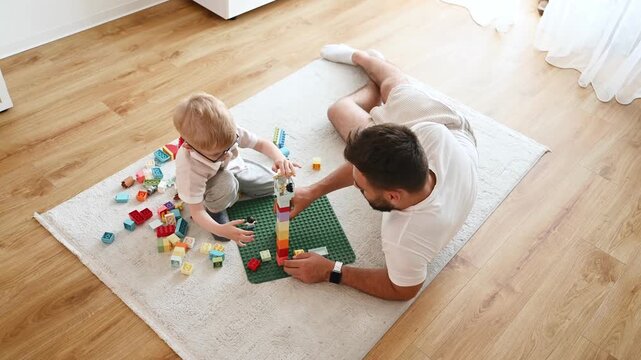 Father is playing in the room with his little son with construction sets.