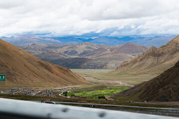 An epic, high-altitude view of a vast mountain valley with a remote village nestled below. Layers...