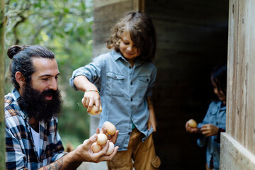 Father with two kids collecting eggs at chicken coop on an organic farm