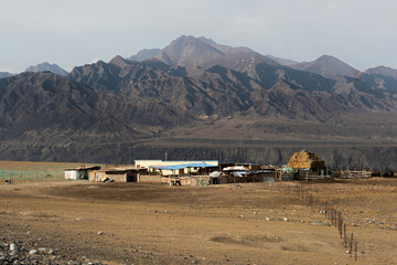 A remote homestead or nomad's settlement in a dry, barren valley. The rustic dwellings are dwarfed...