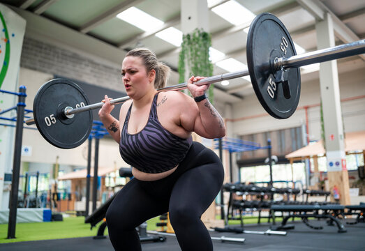 Overweight woman doing squats with barbell in gym