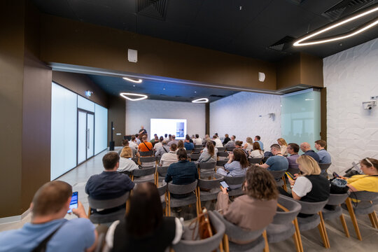 People attending a professional presentation in a modern conference room with a speaker presenting on a screen.