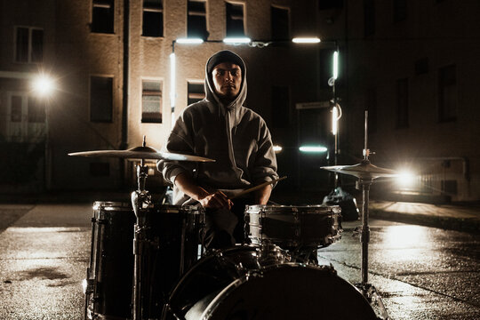 Young male drummer sitting with kit at back yard during night