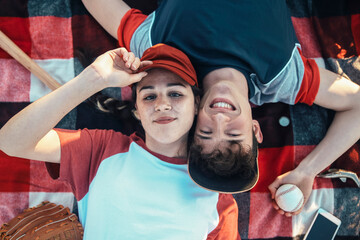 Portrait of smiling young couple with baseball equipment lying on a blanket