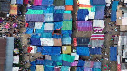 Bogura, Bangladesh - 17 August 2025: Aerial view of a bustling marketplace with colorful tents casting shadows, contrasting with the sandy ground below.