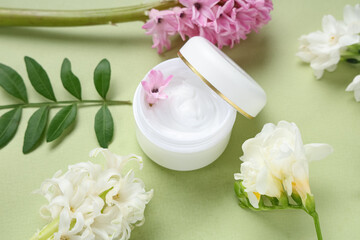 Composition with jar of cream and beautiful flowers on green background
