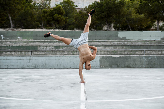 Barechested muscular man doing a handstand on one arm outdoors - Powered by Adobe