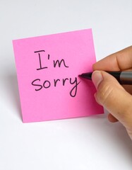 Hand writing 'I'm sorry' on a pink sticky note