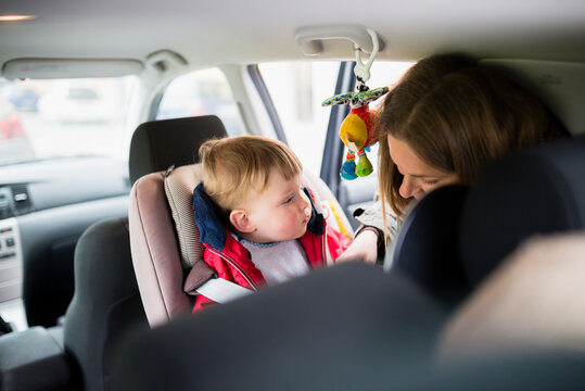 Woman buckling cute son's seat belt in car