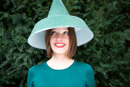 Happy woman with lamp shade on head against plant