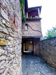 Cobblestone pathway winding beneath stone architecture, wooden balcony adorned with climbing...