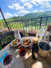 Glasses of red wine and tuscan appetizers served on a table overlooking a beautiful valley in Greve...