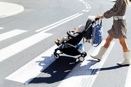 Mother with son in baby carriage on crosswalk in city during sunny day