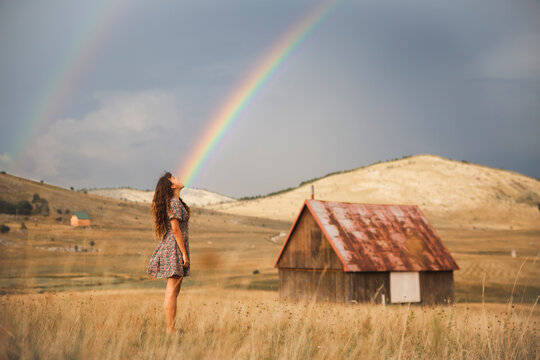 Fototapeta Young woman looking at rainbow standing in meadow