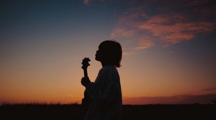 Fototapeta premium Silhouette of a person playing a musical instrument at sunset.
