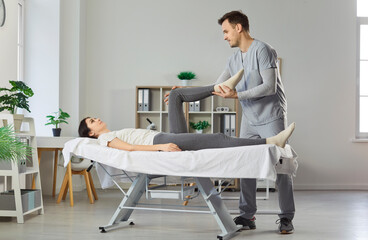 Professional physiotherapist doing massage of legs to woman patient who is lying on couch, help to deal with pain, doing manual therapy in medical clinic, helping to maintain body health