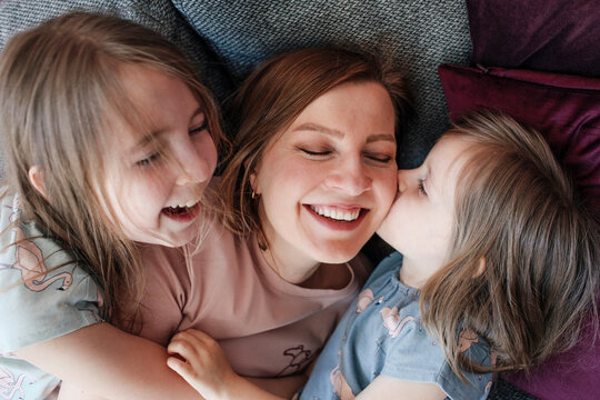 Happy daughters embracing mother while lying down on couch at home