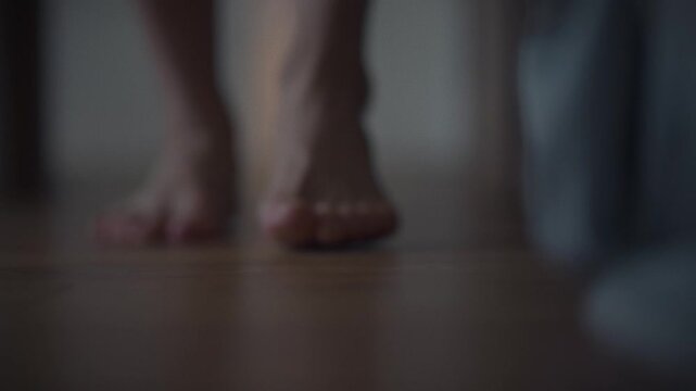 A man slowly walks barefoot on wooden planks in a softly lit room. The soft light envelops the feet, creating a feeling of quiet evening coziness. This scene gives a feeling of peace and inner harmony