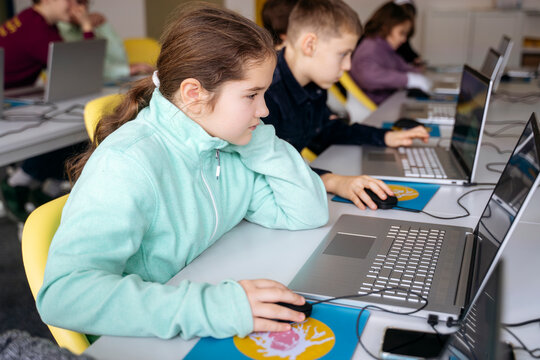 Dedicated girl using laptop learning computer programming at desk in school classroom